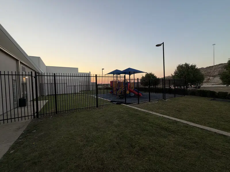 Black ornamental metal fence enclosing a playground at a Fort Worth, TX commercial facility